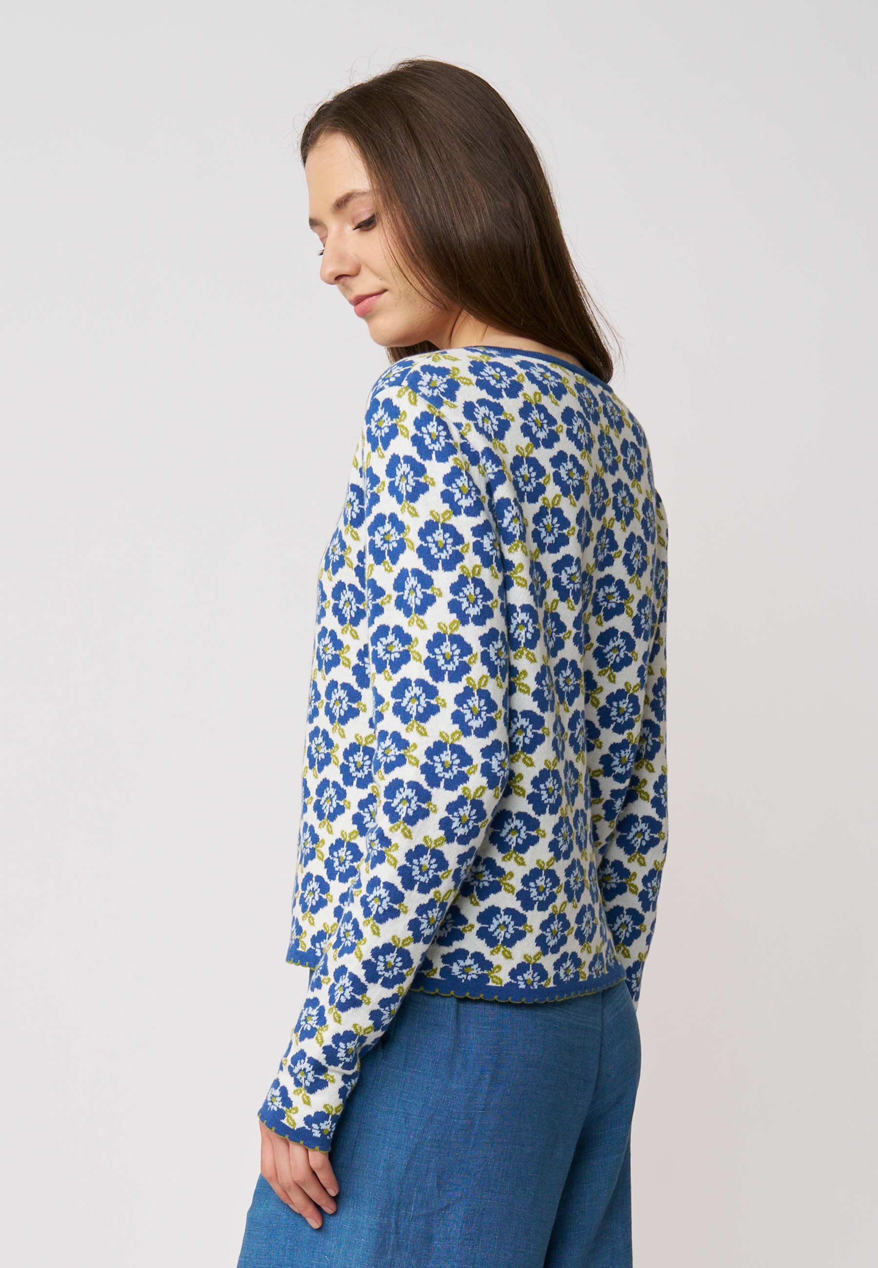 Frau trägt Strickjacke, Modell Juliana, mit blauem Blumenmuster auf hellem Grund vor schlichtem Hintergrund