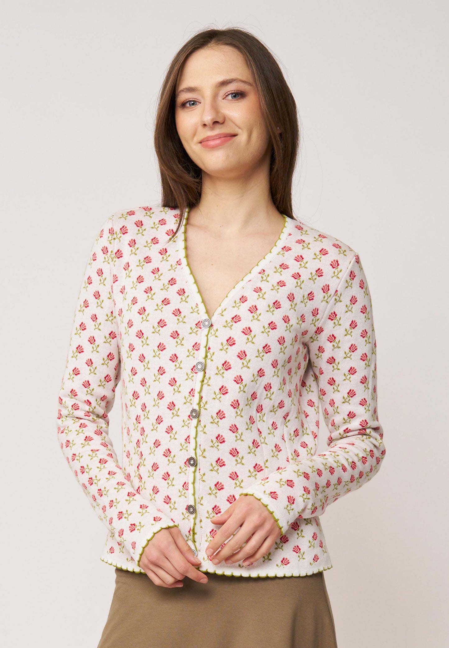 Frau trägt Strickjacke, Modell Lucien, in hellem Ecru mit kleinem rosaroten Blumenmuster und grünem Zierabschluss vorne