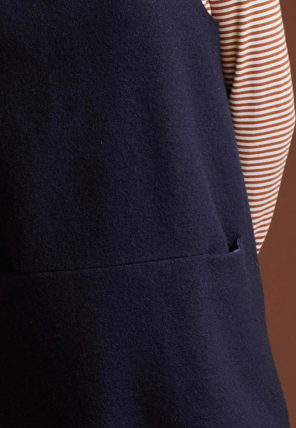 Trägerkleid, Modell Liza in Dunkelblau über gestreiftem Shirt vor braunem Hintergrund