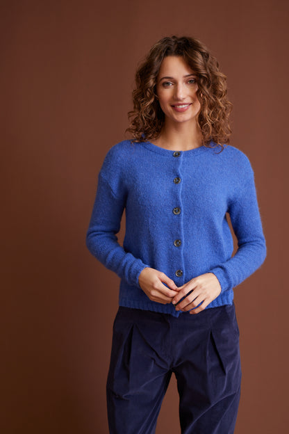 Frau trägt Jacke, Modell Nikola in Blau aus weichem Material, kombiniert mit dunkler Hose vor braunem Hintergrund