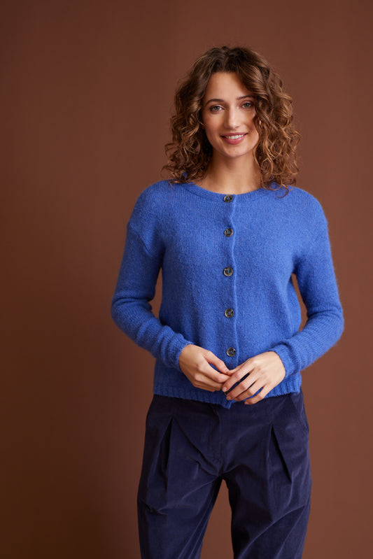 Frau trägt Jacke, Modell Nikola in Blau aus weichem Material, kombiniert mit dunkler Hose vor braunem Hintergrund